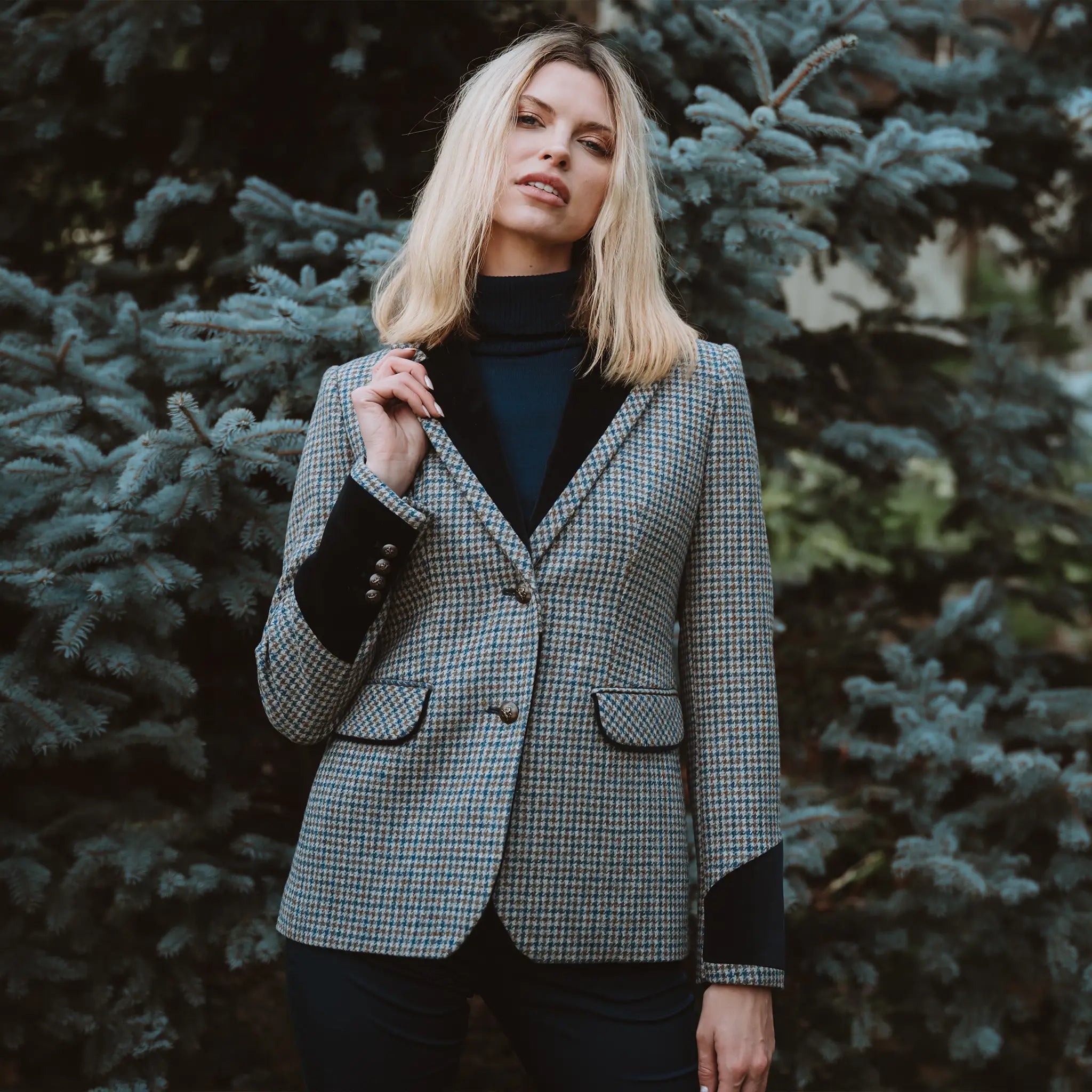 Grantham Midnight Check Wool Jacket by Welligogs, front view on a model beside evergreen trees, showing the check pattern, velvet lapels, and contrast cuffs.