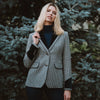 Grantham Midnight Check Wool Jacket by Welligogs, front view on a model beside evergreen trees, showing the check pattern, velvet lapels, and contrast cuffs.