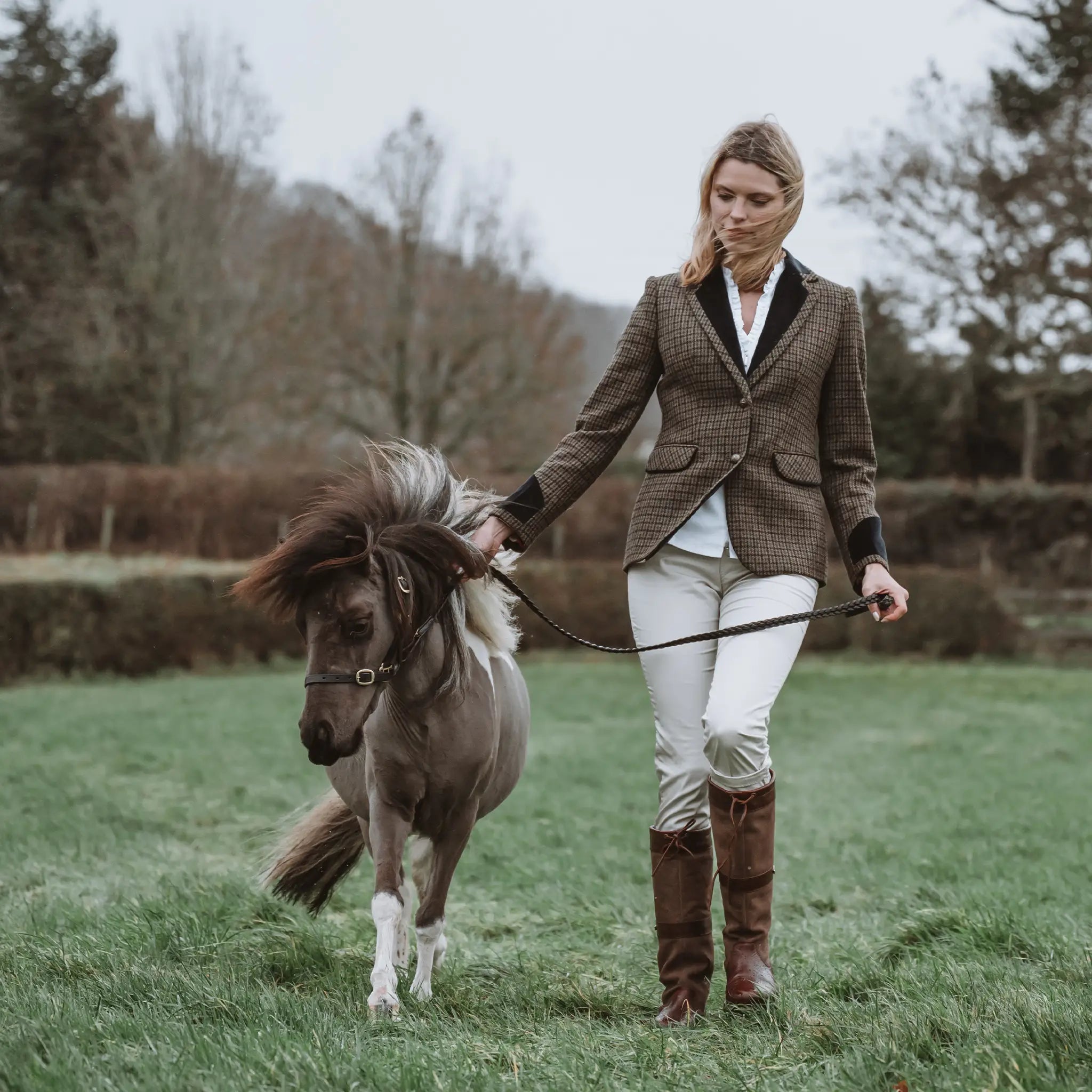 Grantham Sage Check Wool Jacket by Welligogs, full-length outdoor view on a model leading a pony, showing the tailored silhouette.