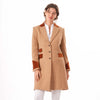 A woman modeling the Welligogs Damelza Camel Coat - a wool coat with brown suede-like trim on the collar, cuffs, and pockets, worn over a white blouse and white trousers against a plain white background.