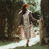 Woman in a floral dress and hat standing in a garden