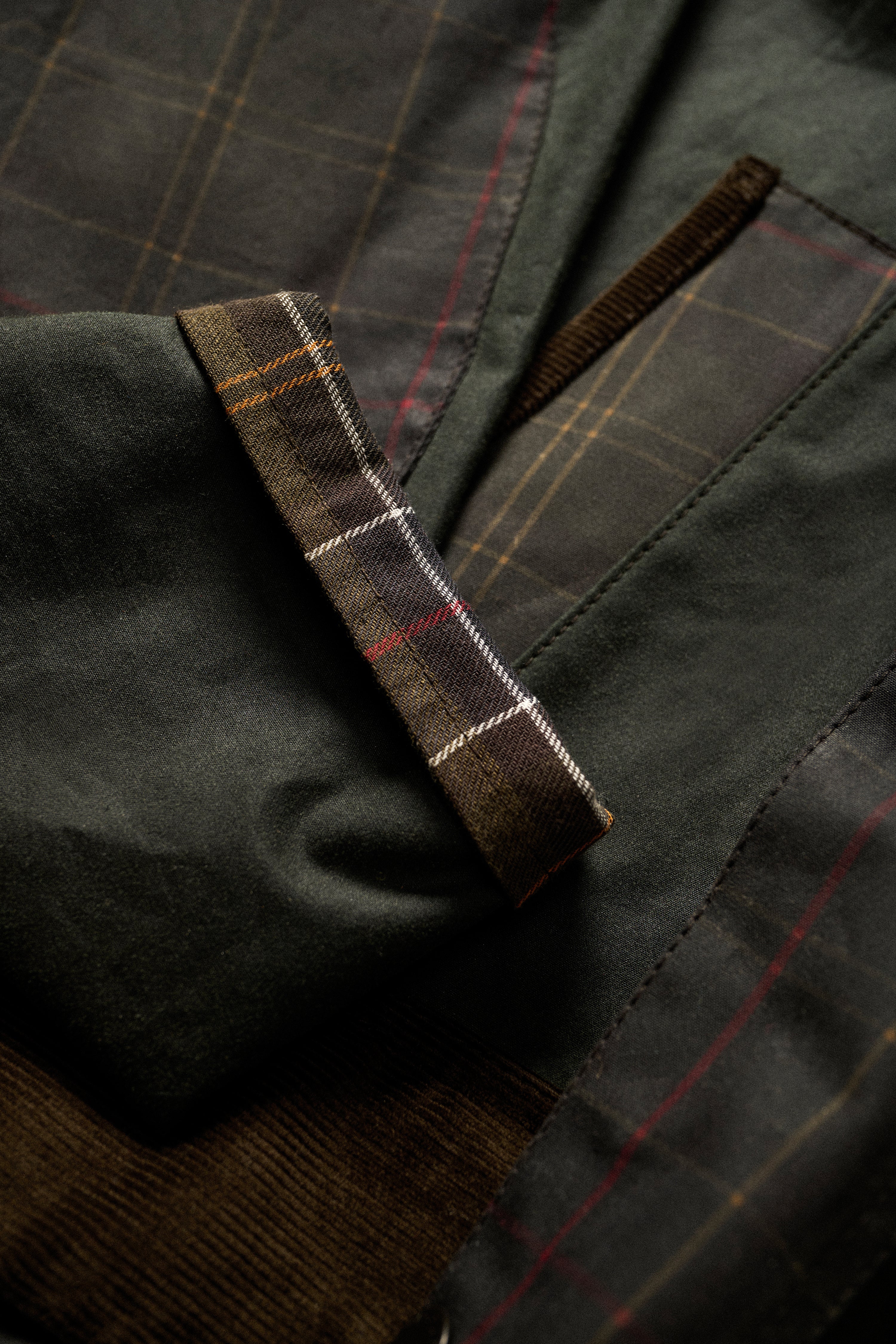 Close-up detail of the Barbour Icons Patch Bedale Wax Jacket showing the tartan patch lining, waxed cotton fabric, and corduroy trim at the cuff and pocket.