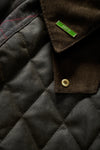Close-up of a dark brown corduroy collar with a gold snap button and a small green brand tag reading 'SPEY', next to a dark quilted fabric panel.