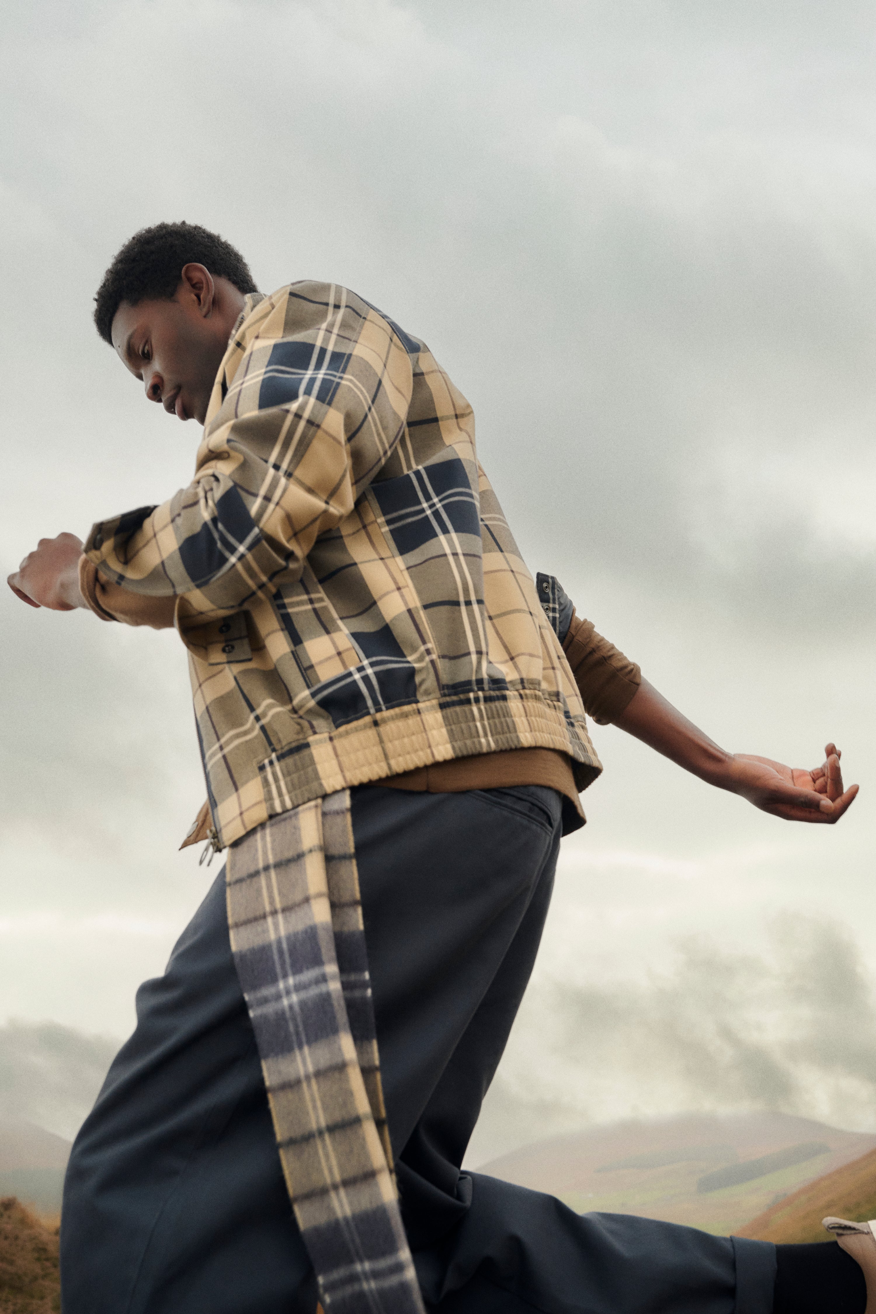 A man outdoors wearing a beige and navy plaid jacket - a Barbour Tartan Showerproof Blouson Jacket.