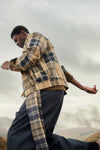 A man outdoors wearing a beige and navy plaid jacket - a Barbour Tartan Showerproof Blouson Jacket.