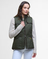 Woman wearing a green quilted vest over a light gray sweater on a white background