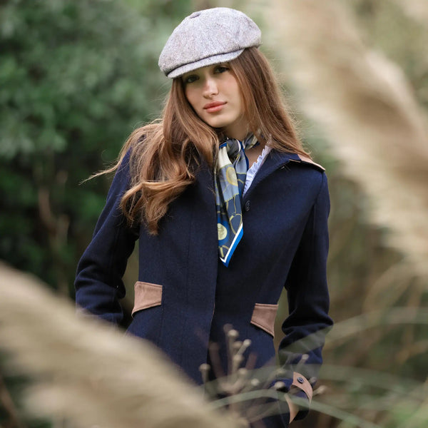 Woman wearing a navy coat, gray cap, and patterned scarf outdoors.