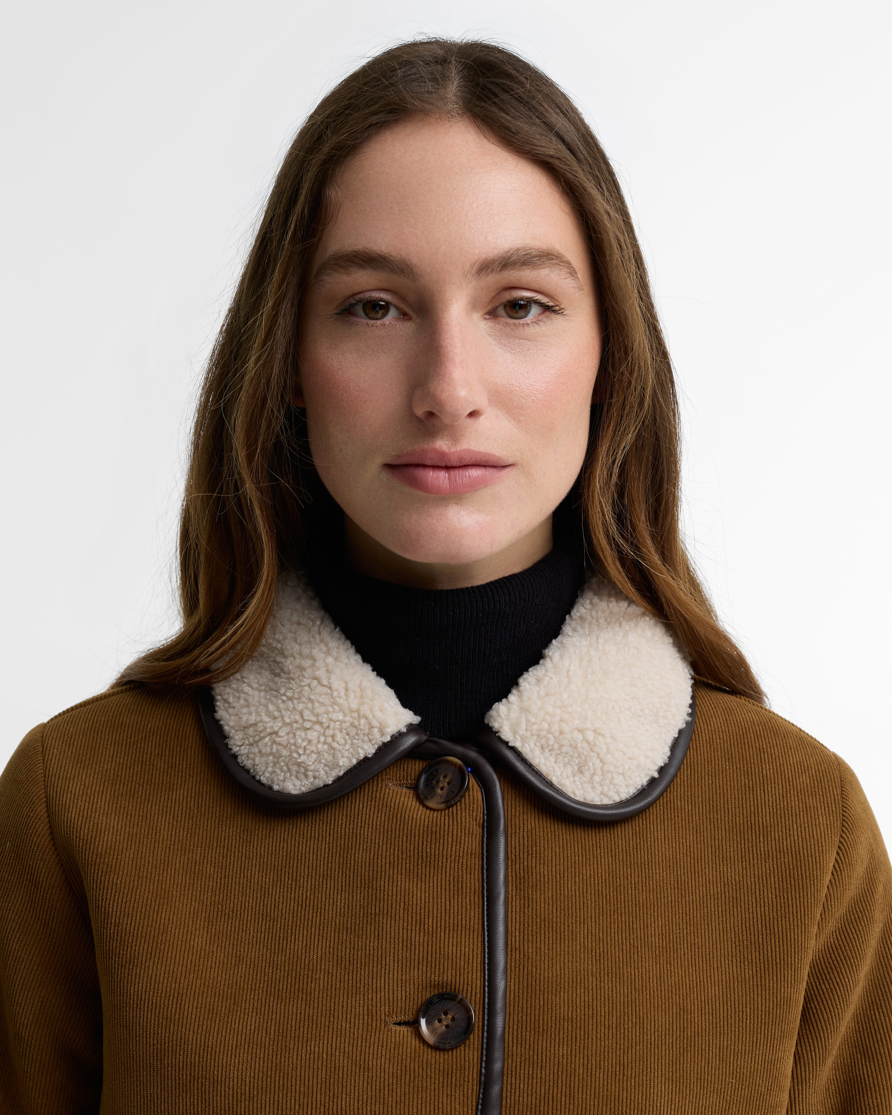 Woman wearing a brown coat with a black and white collar against a white background