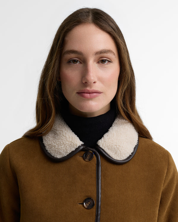 Woman wearing a brown coat with a black and white collar against a white background