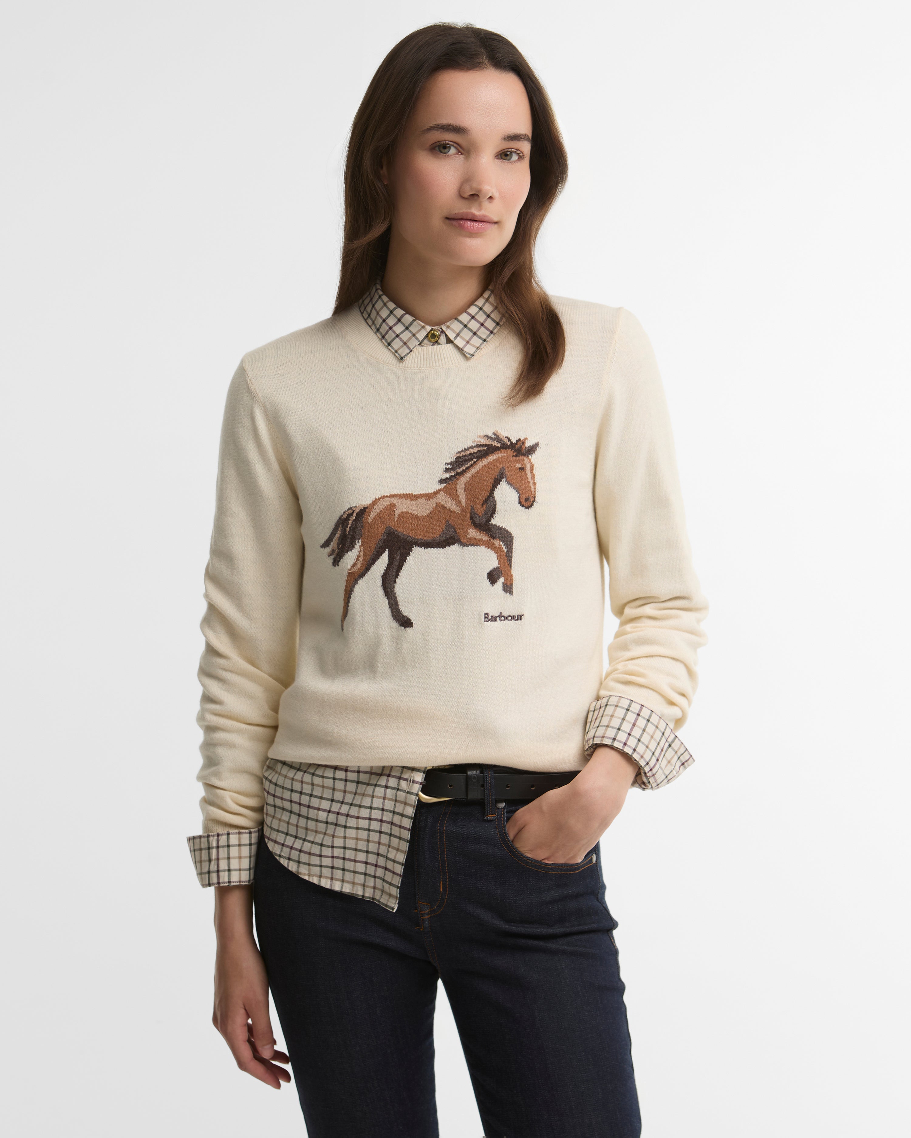 Woman wearing a cream sweater with a horse design on a plain background