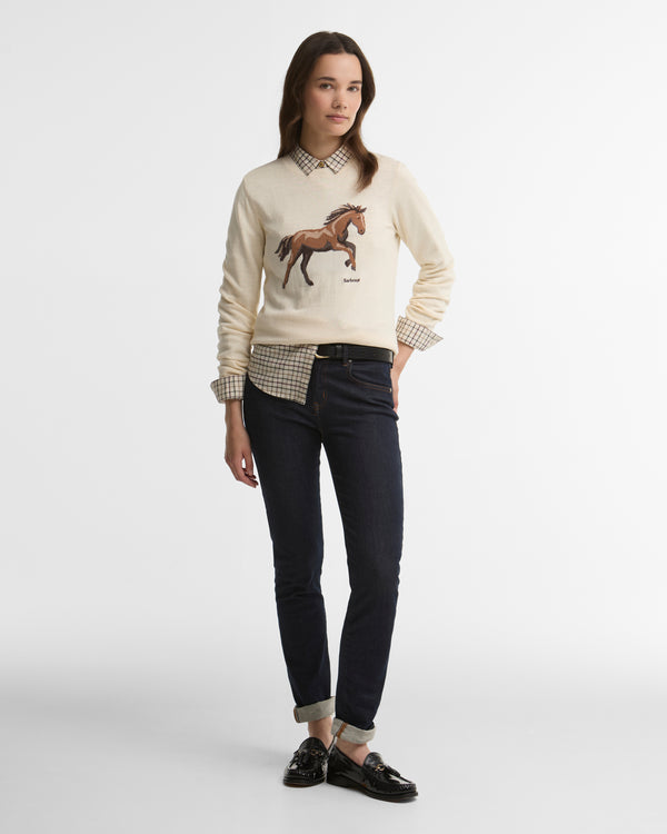 Woman wearing a cream sweater with a horse design, checkered shirt, and black pants on a white background