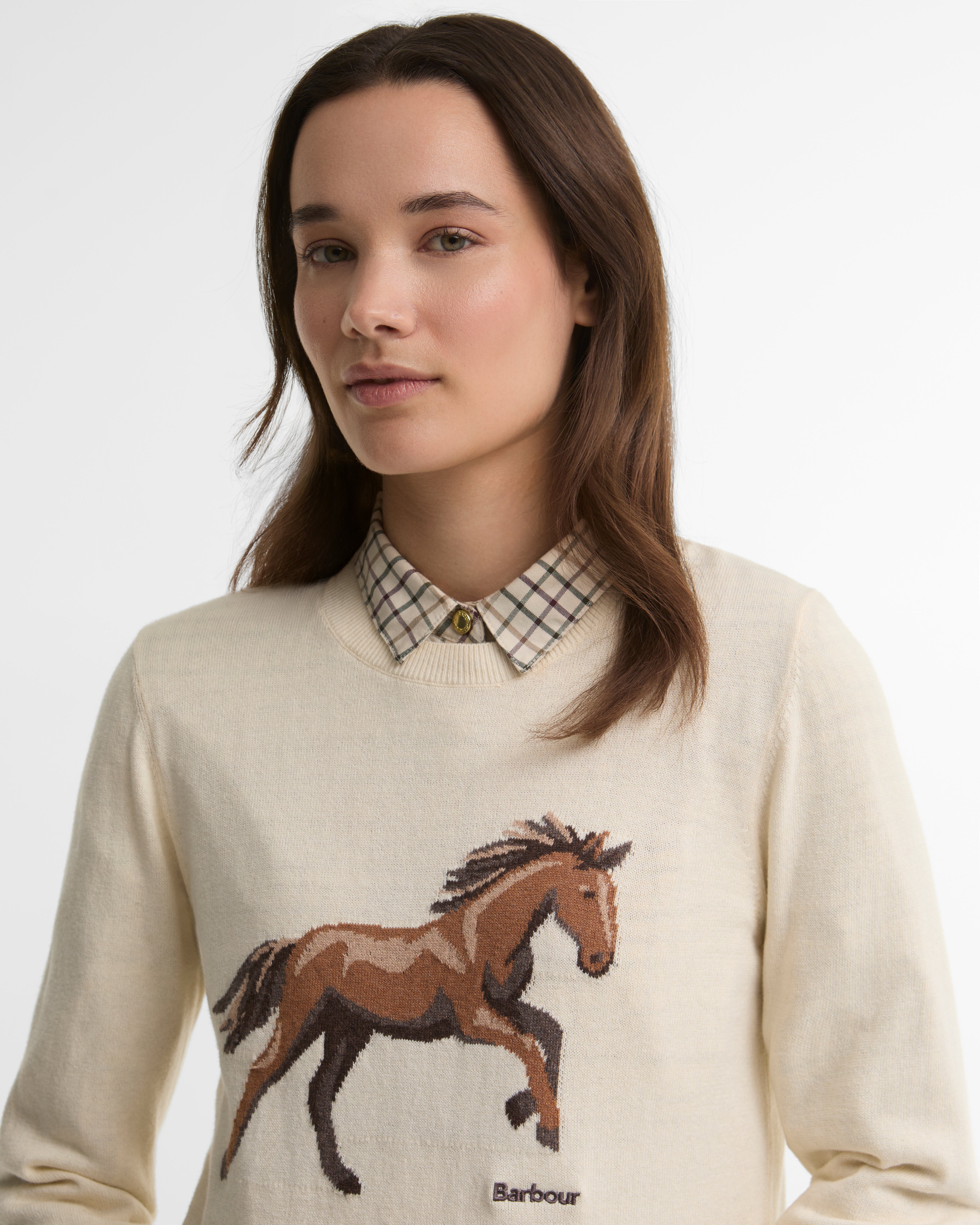 Woman wearing a cream sweater with a horse design and Barbour logo.