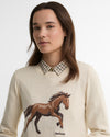 Woman wearing a cream sweater with a horse design and Barbour logo.