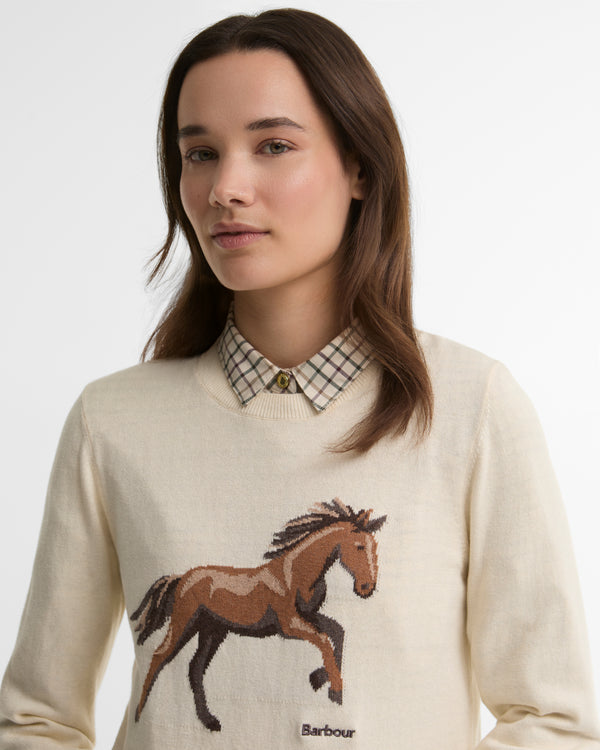 Woman wearing a cream sweater with a horse design and Barbour logo.