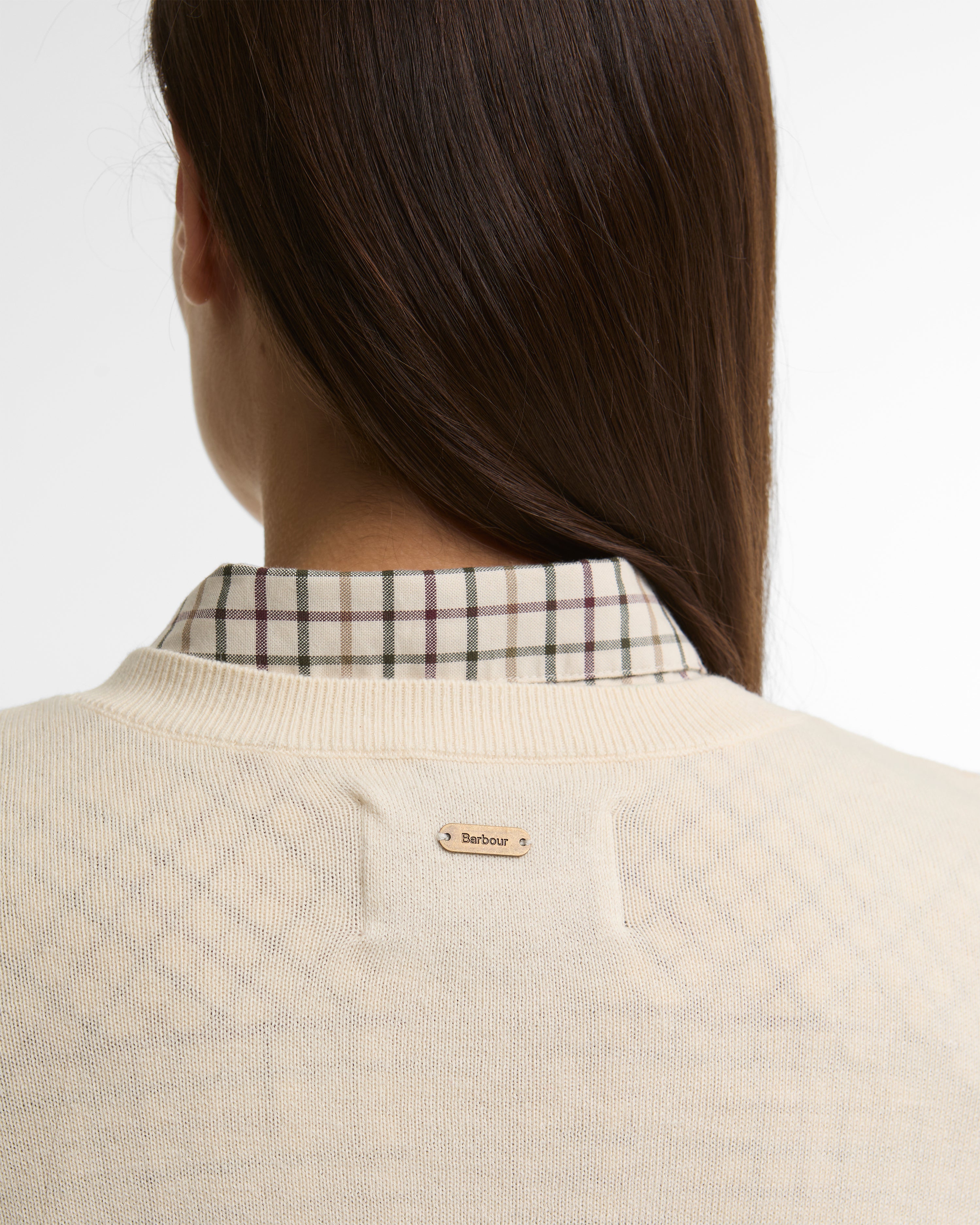 Person wearing a beige sweater with a plaid shirt underneath, on a plain background