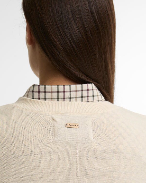 Person wearing a beige sweater with a plaid shirt underneath, on a plain background