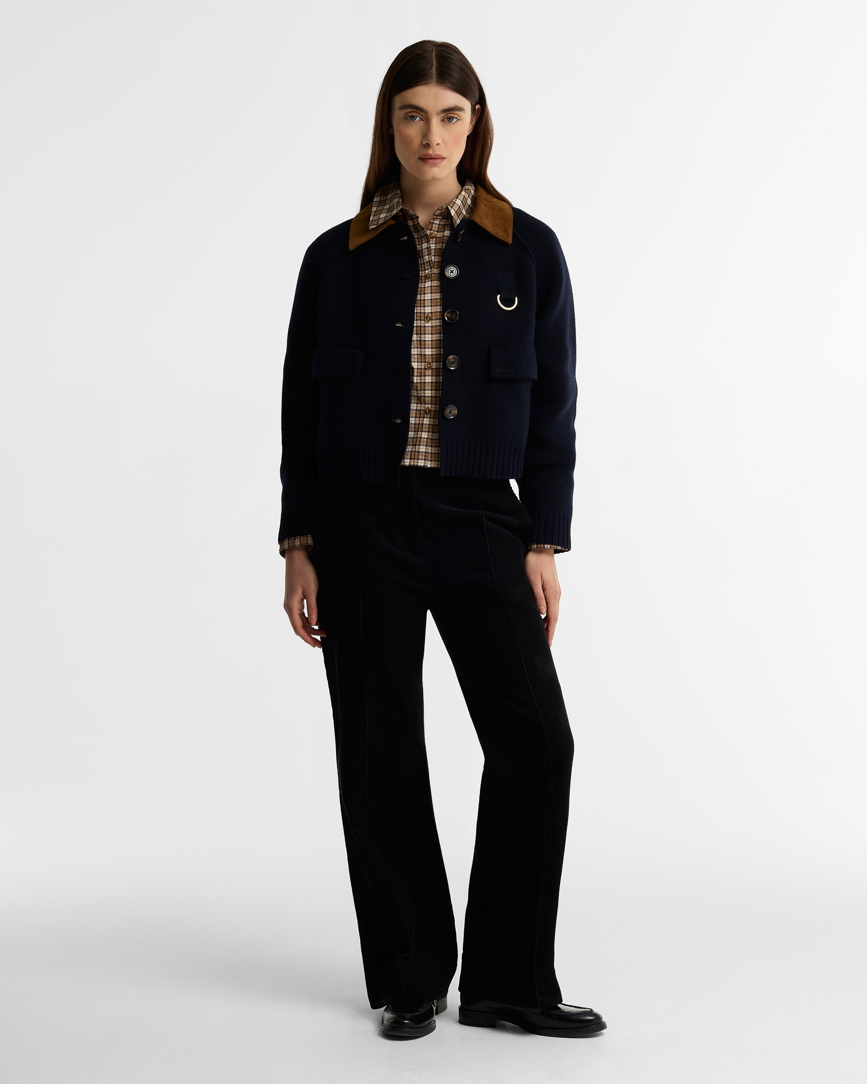 Person wearing a dark coat with plaid collar and black pants on a white background