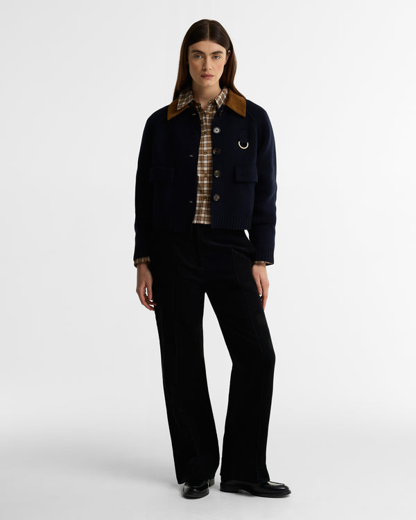 Person wearing a dark coat with plaid collar and black pants on a white background