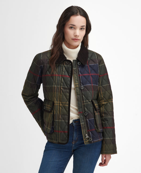 A woman modeling a quilted plaid jacket with a dark brown collar, worn over a cream turtleneck and blue jeans, against a plain white studio background.