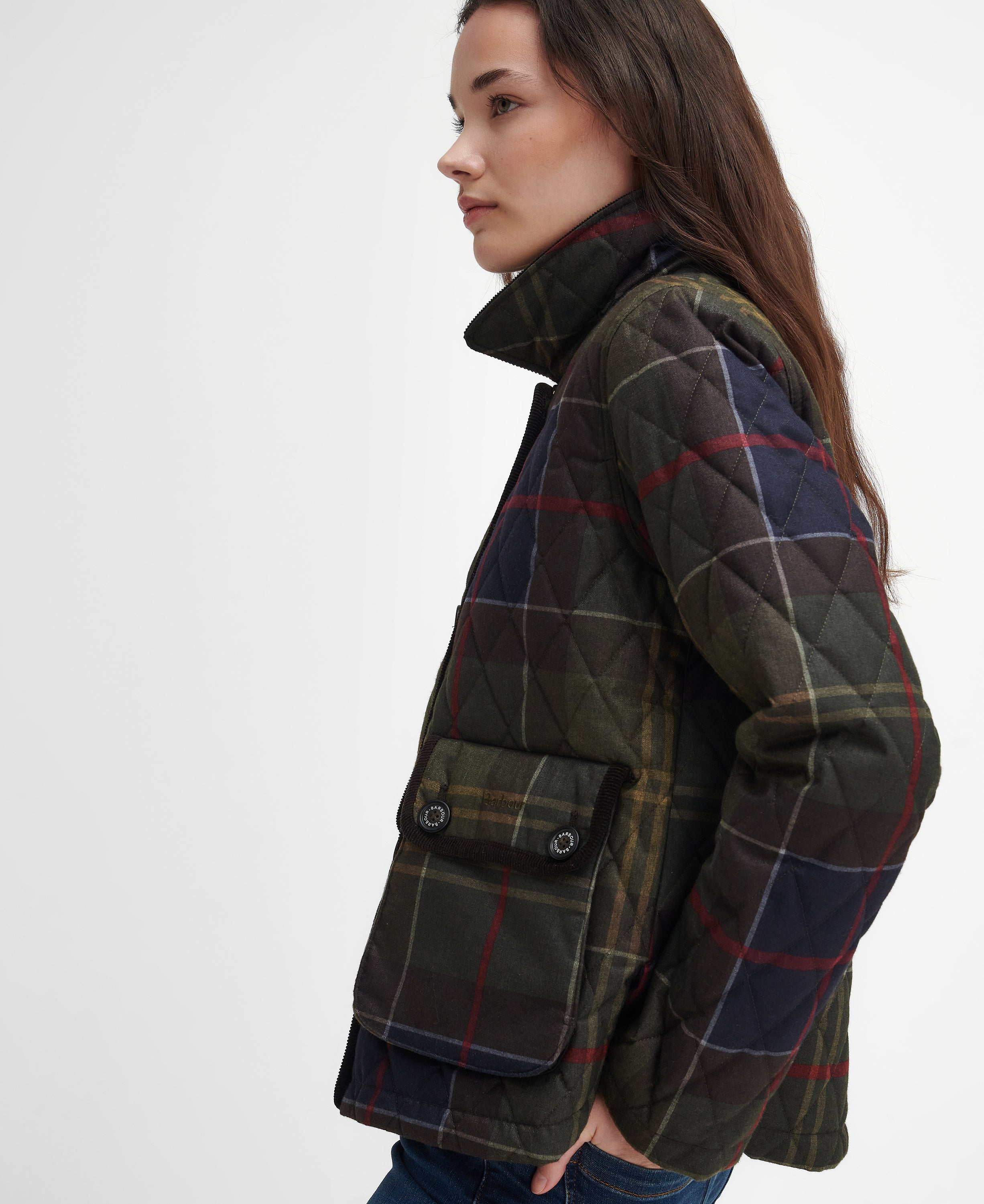 A woman shown in profile wearing a quilted plaid jacket. The jacket features a dark green base with a classic tartan pattern in red, blue, and yellow, with solid dark green quilted shoulder panels.
