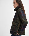 A woman shown in profile wearing a quilted plaid jacket. The jacket features a dark green base with a classic tartan pattern in red, blue, and yellow, with solid dark green quilted shoulder panels.