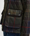 Close-up of a quilted Barbour jacket in a green and brown plaid pattern, featuring a front flap pocket with snap buttons and the Barbour logo.