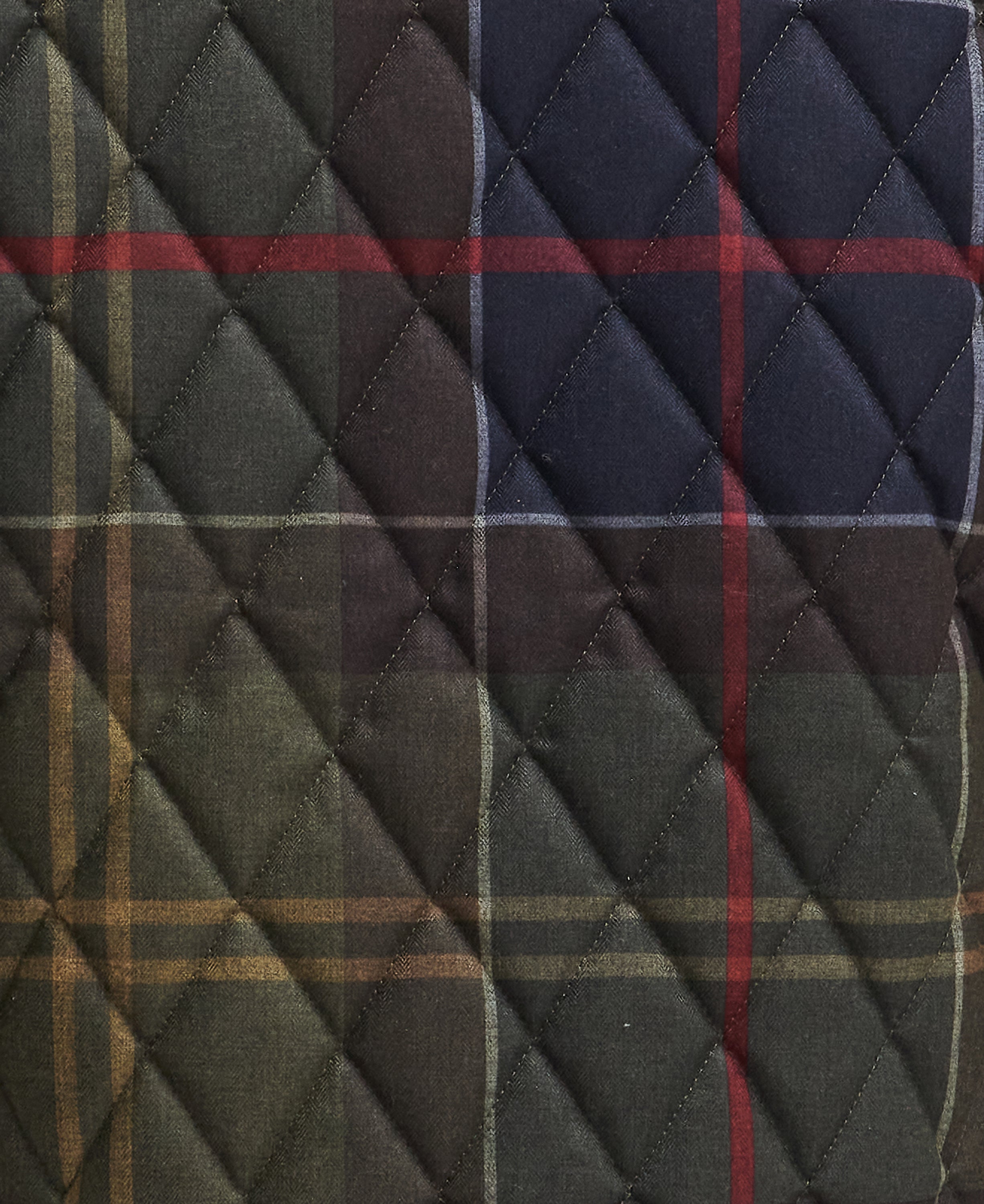 A close-up of a quilted fabric with a tartan plaid pattern in dark green, navy blue, brown, and red, featuring diamond-quilted stitching.