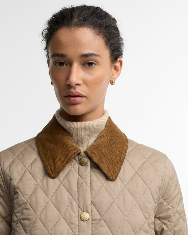 A close-up of a model wearing a beige quilted jacket with a contrasting brown suede collar, layered over a cream turtleneck sweater.