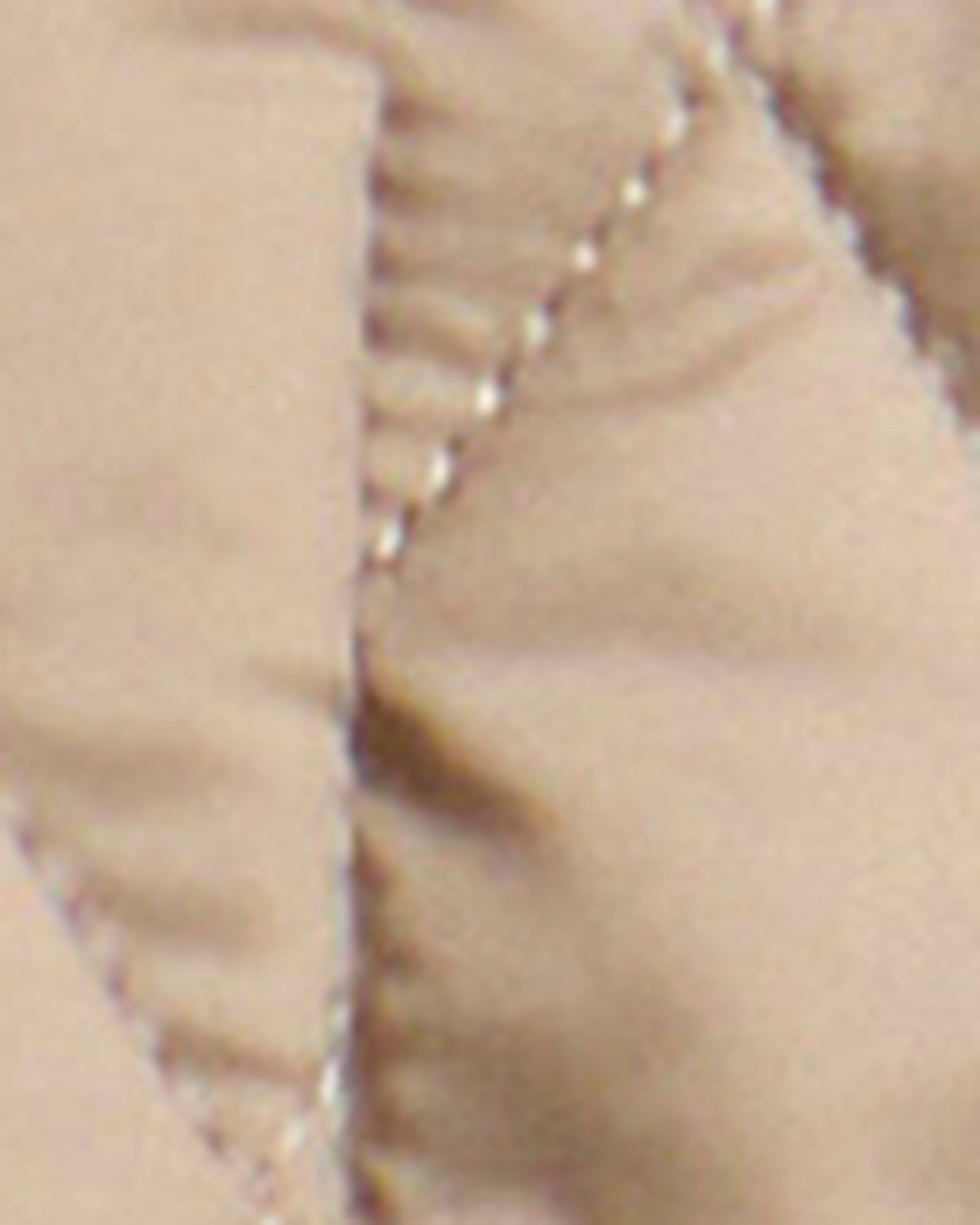 Close-up of a quilted fabric surface in a warm beige or light tan color, showing stitched paneling and stitching detail.