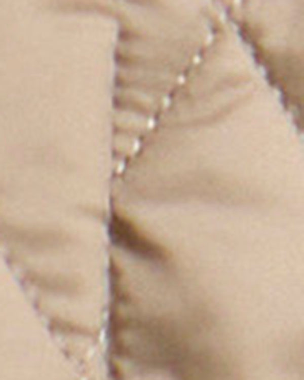 Close-up of a quilted fabric surface in a warm beige or light tan color, showing stitched paneling and stitching detail.
