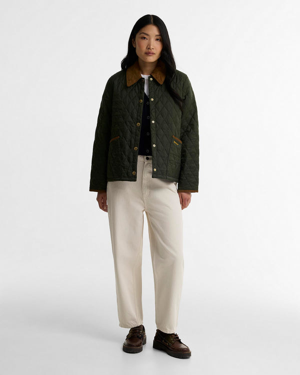 A model stands against a light gray studio background wearing a dark olive green quilted jacket with a brown collar, cream wide-leg trousers, and dark brown shoes.