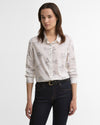 A woman modeling a long-sleeve button-up shirt with a delicate horse pattern, paired with dark blue jeans and a black belt, against a plain white studio background.