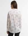 A woman viewed from the back wearing a white long-sleeve button-up shirt with a black horse line-art pattern, paired with dark pants, against a plain light gray studio background.