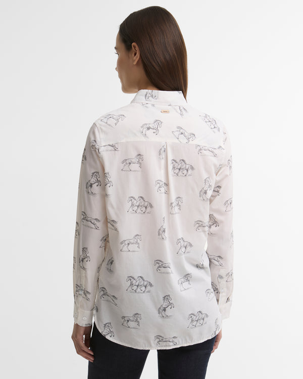 A woman viewed from the back wearing a white long-sleeve button-up shirt with a black horse line-art pattern, paired with dark pants, against a plain light gray studio background.