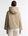 A person shown from the back wearing a light beige hooded jacket and cream pants against a clean white studio background.