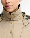 Close-up of a model wearing a beige high-collar jacket with gold-tone snap buttons and a patterned lining visible at the collar.