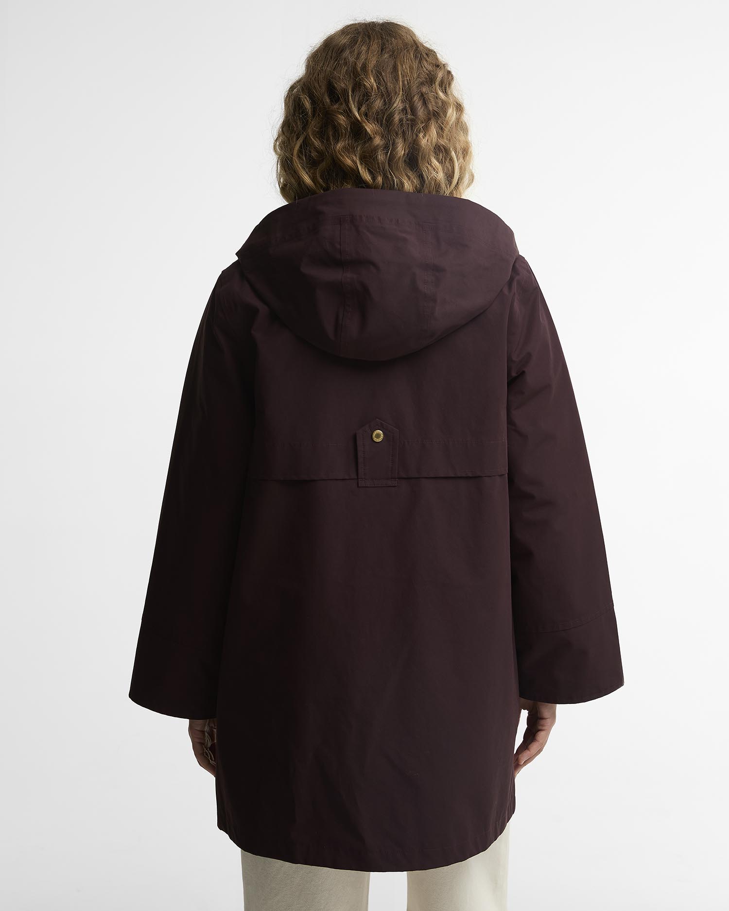 A person viewed from the back wearing a hooded jacket in a deep burgundy or maroon shade, paired with light beige pants, against a plain light gray studio background. A single gold-colored button detail is centered on the back.