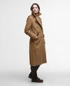 A woman modeling a mid-length camel brown double-breasted wool coat with a high collar, paired with dark brown leather boots, against a plain light gray studio background.