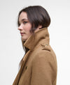 A woman shown in profile wearing a camel brown wool coat with a high collar, photographed against a clean white studio background.