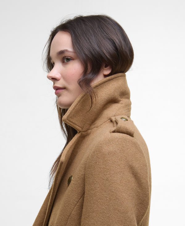 A woman shown in profile wearing a camel brown wool coat with a high collar, photographed against a clean white studio background.