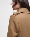 Close-up side profile of a model wearing a camel brown wool coat with a structured collar and a single decorative button, set against a plain light gray background.