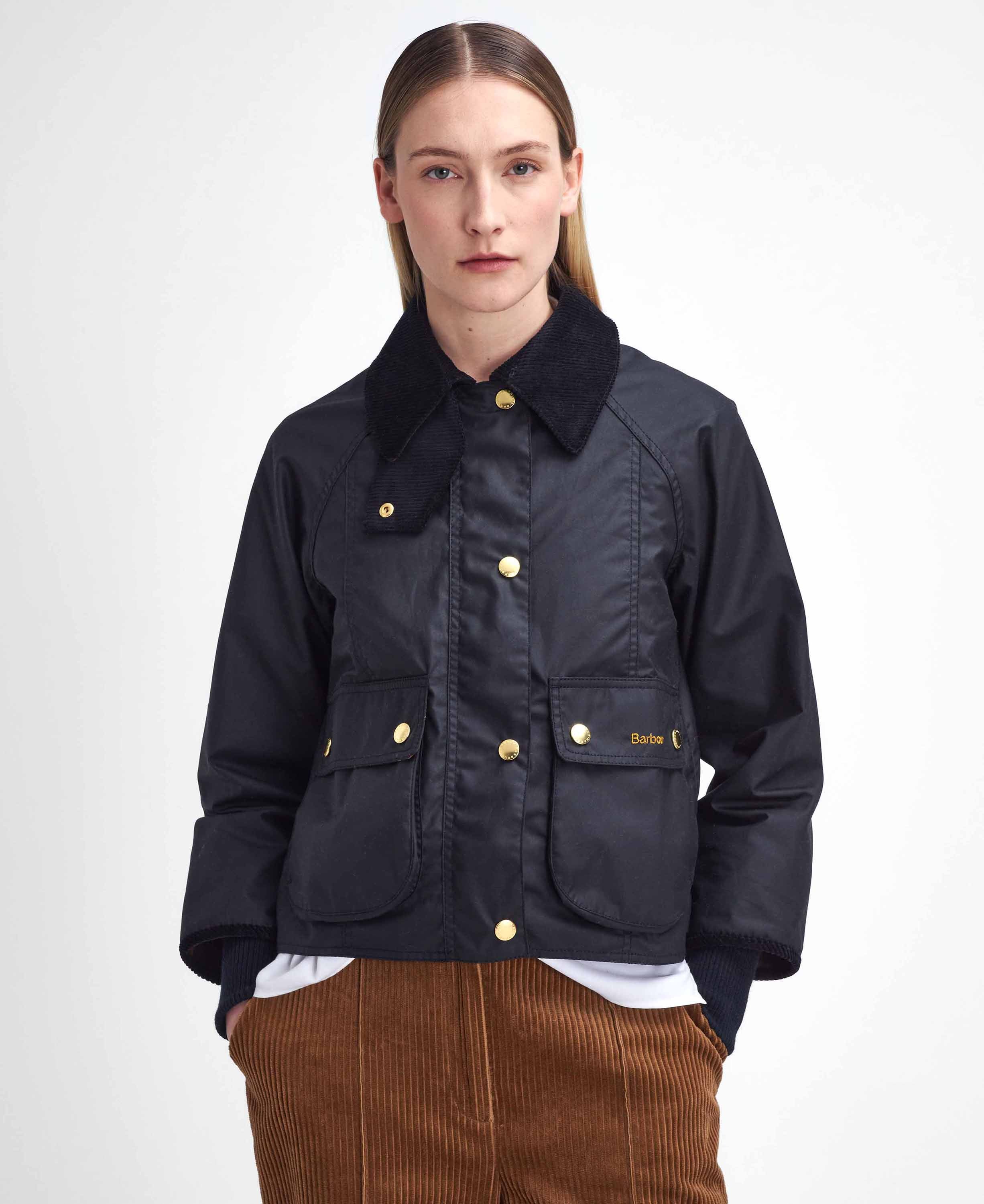 A model wearing a black waxed cotton jacket with a black corduroy collar and gold-tone buttons, paired with brown corduroy trousers, against a plain white studio background.