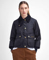 A model wearing a black waxed cotton jacket with a black corduroy collar and gold-tone buttons, paired with brown corduroy trousers, against a plain white studio background.