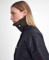 A side-profile view of a woman wearing a black waterproof jacket with a high collar and a plaid lining in green, brown, and orange, set against a plain light gray background.