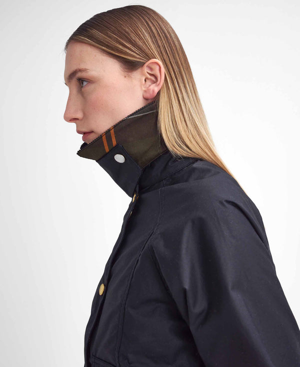 A side-profile view of a woman wearing a black waterproof jacket with a high collar and a plaid lining in green, brown, and orange, set against a plain light gray background.