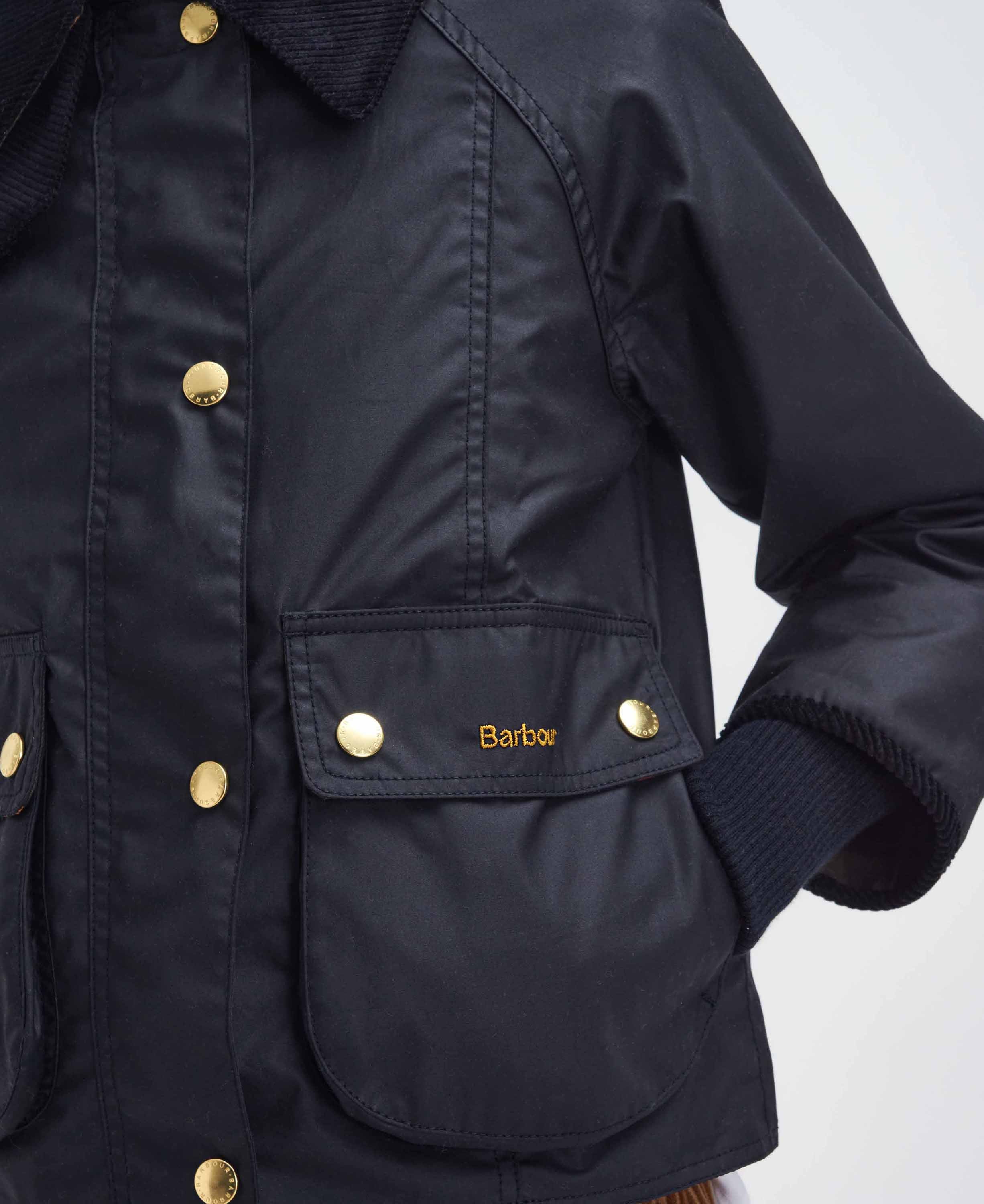 Close-up of a black waxed cotton jacket with gold-tone buttons and the Barbour logo embroidered on a front pocket flap.