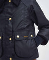 Close-up of a black waxed cotton jacket with gold-tone buttons and the Barbour logo embroidered on a front pocket flap.