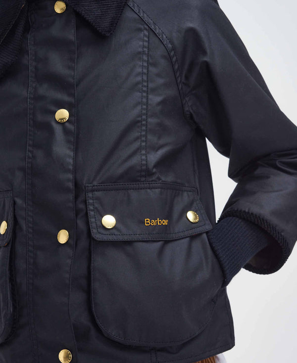 Close-up of a black waxed cotton jacket with gold-tone buttons and the Barbour logo embroidered on a front pocket flap.