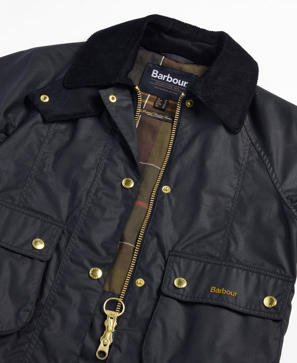 Close-up of a Barbour waxed jacket in black, featuring a black corduroy collar, gold-tone snap and zipper hardware, and a plaid lining visible at the open collar.