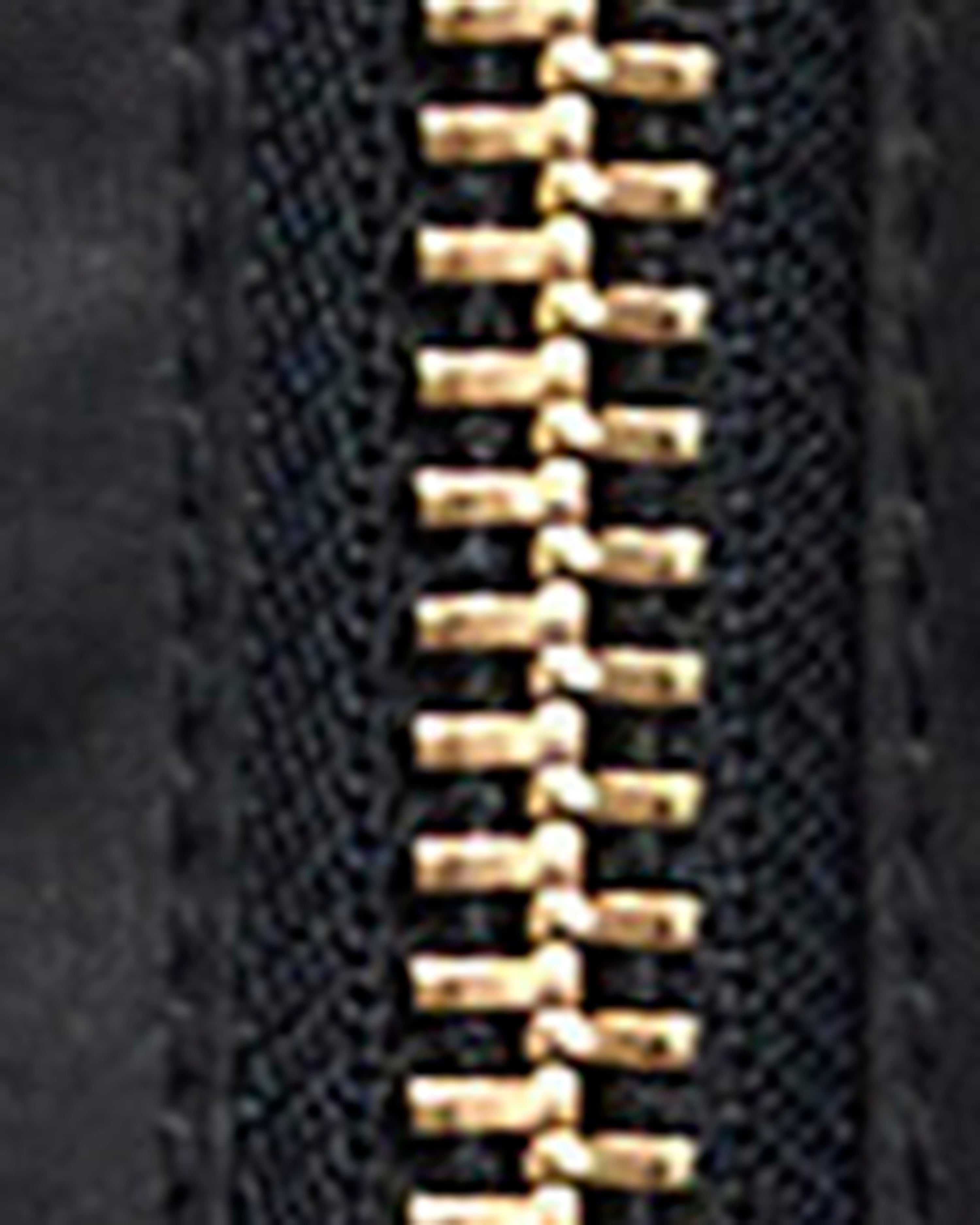 Close-up of a black zipper with gold-toned metal teeth on a dark textured fabric background.